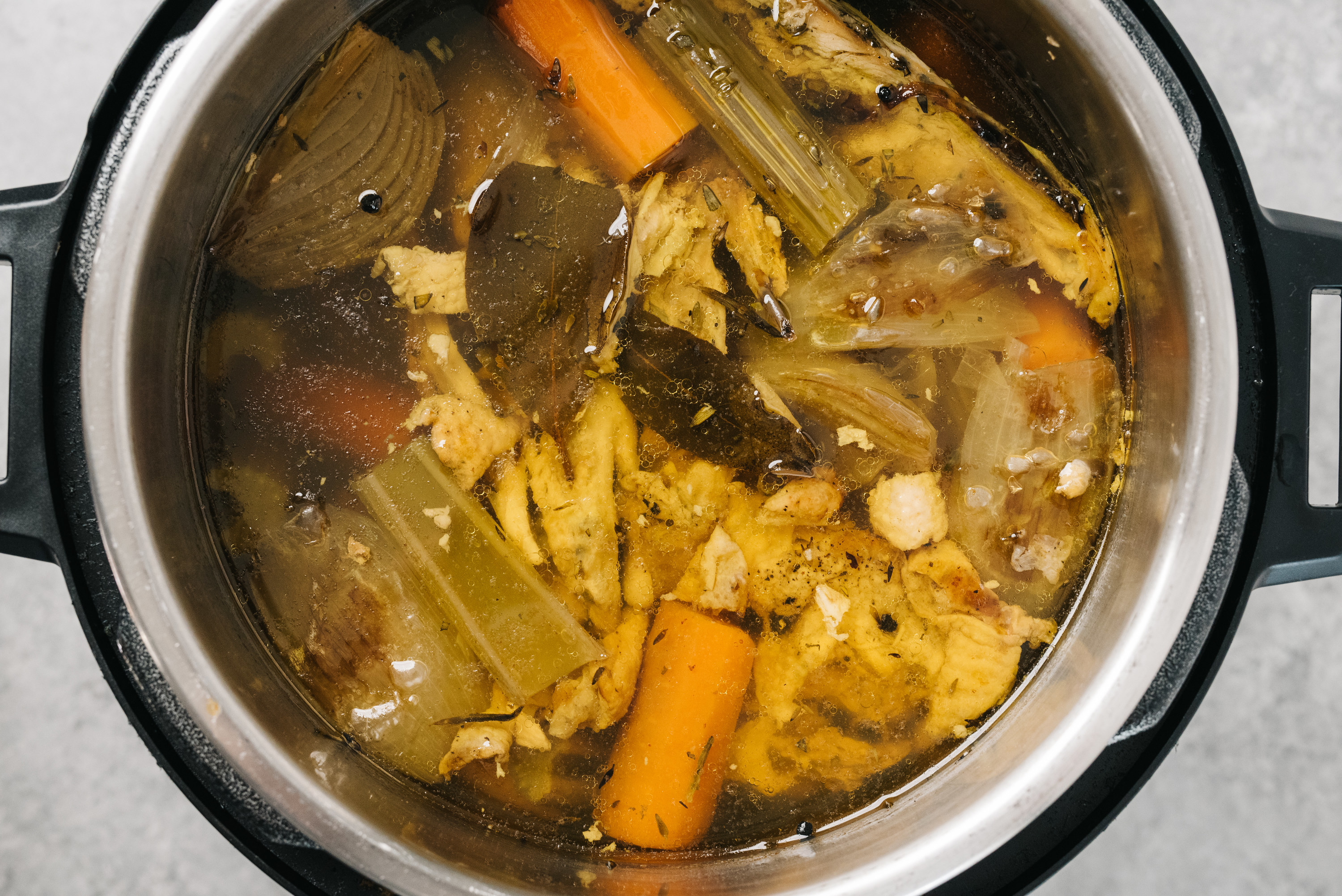 instant pot full of chicken stock and various veggies and herbs