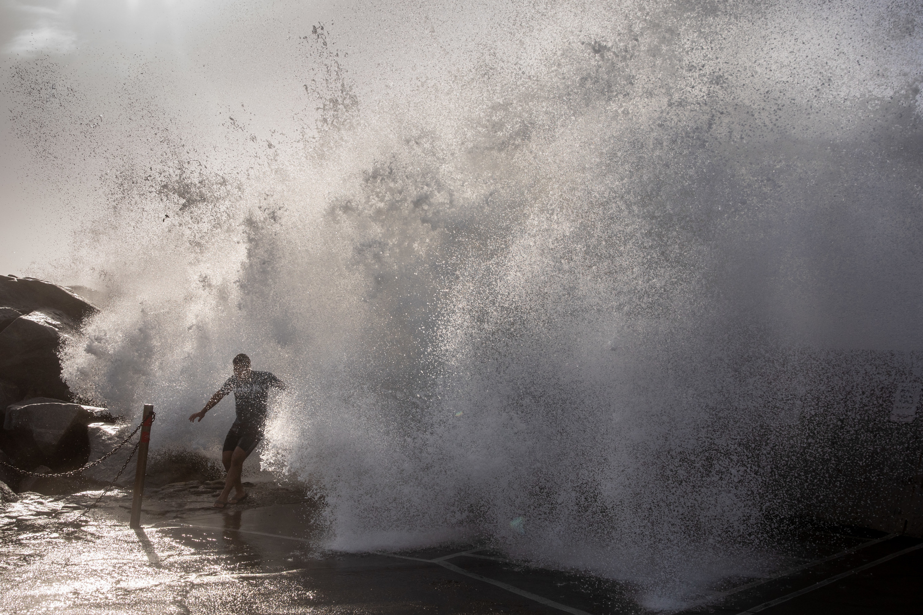 A man running from a large wave crash by the sea.