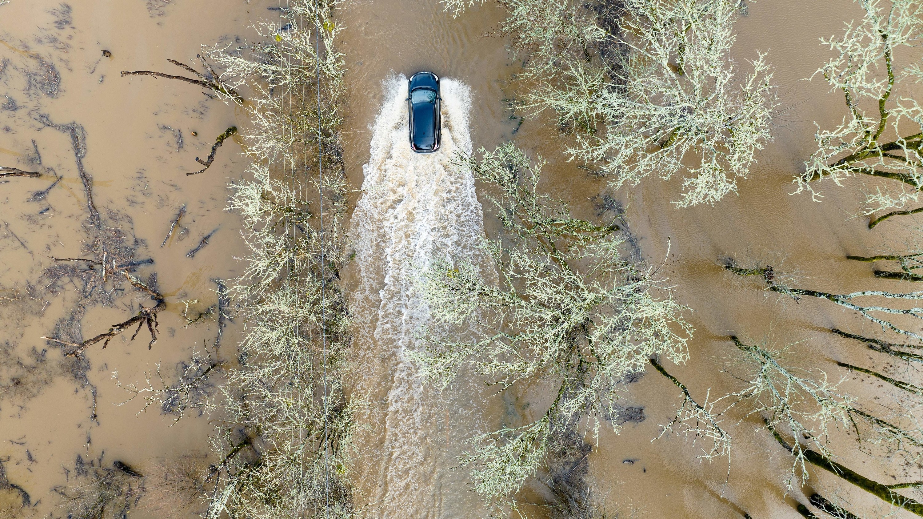 A topshot of a car driving through deep muddy water.