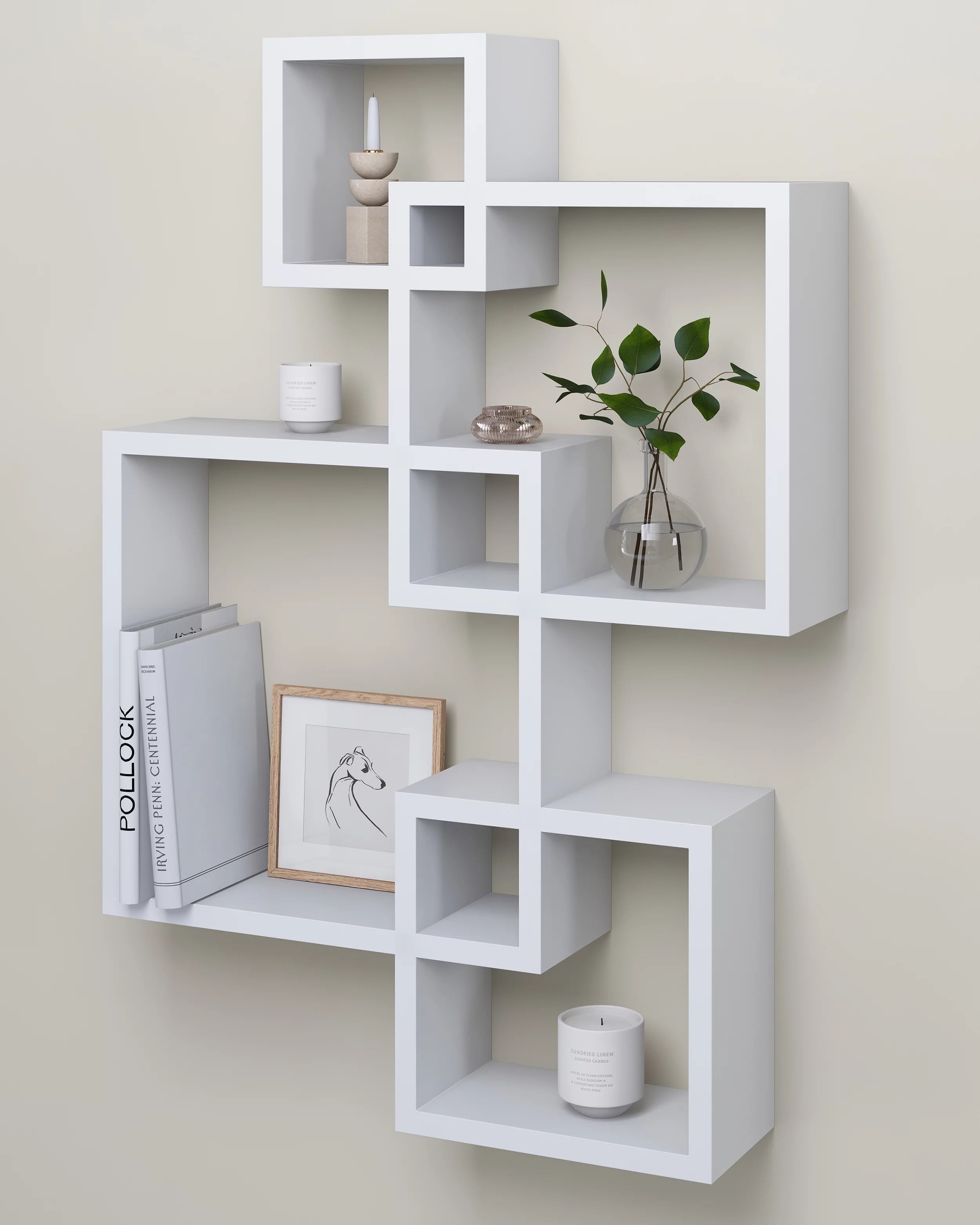 a white four-cube hanging shelf holding books, candles, and a plant