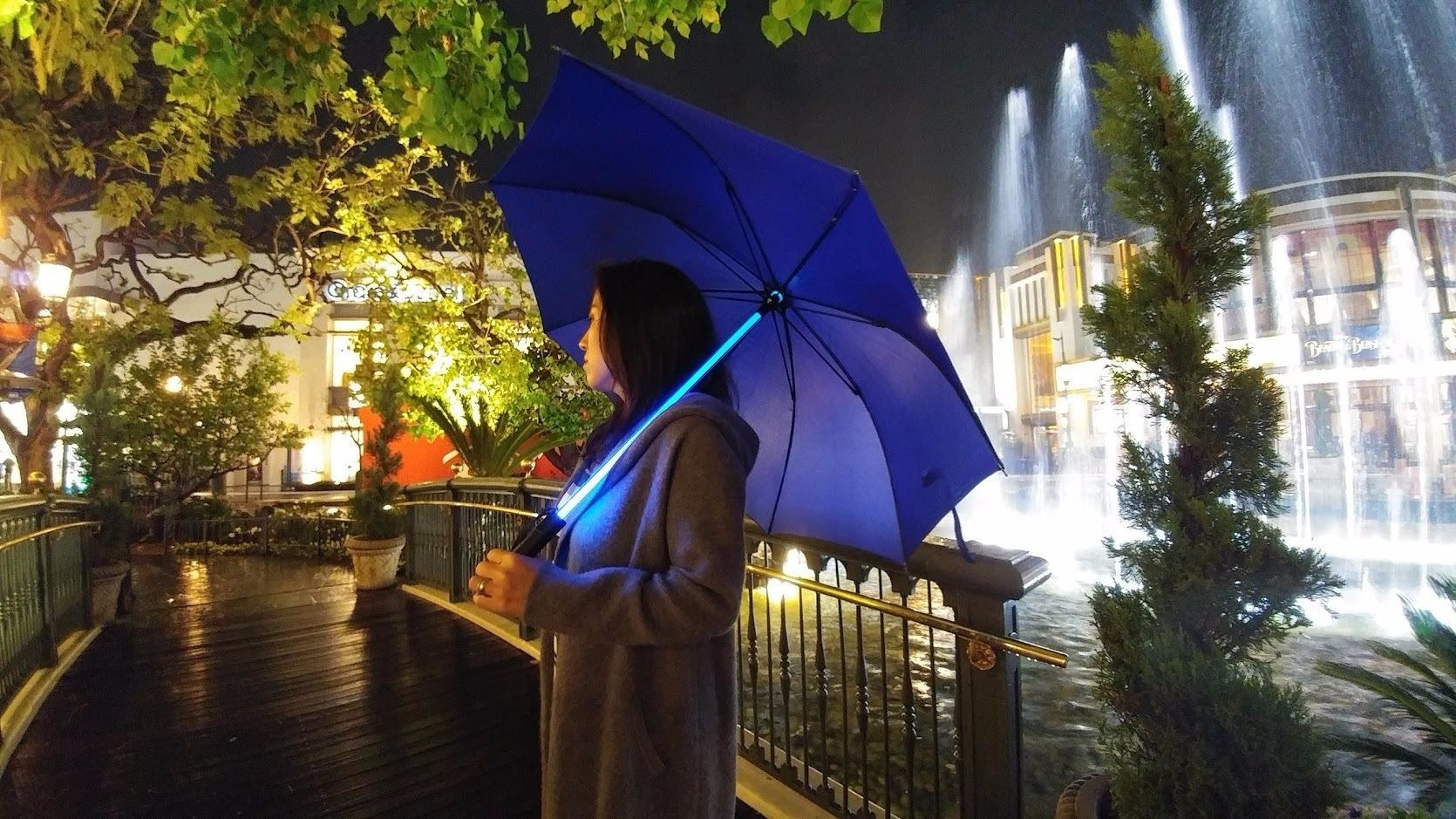 A person holding the umbrella, which has a shaft that glows like a lightsaber