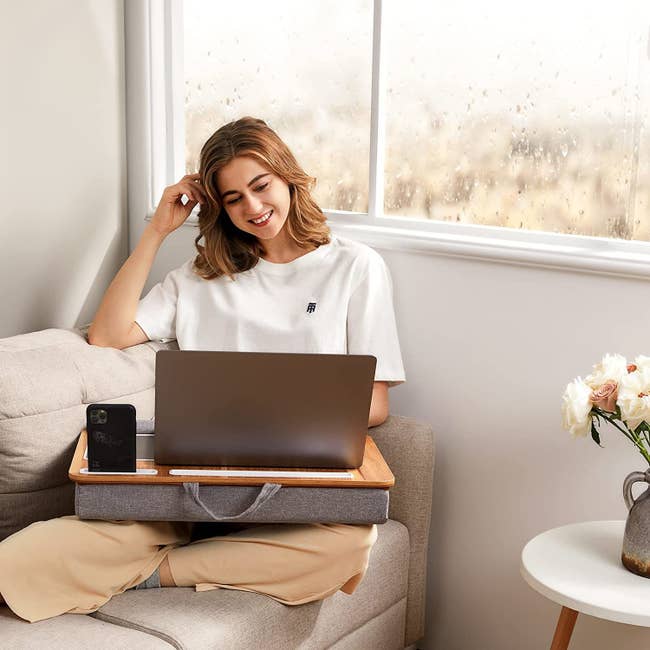 model sitting connected sofa utilizing laptop with thigh desk