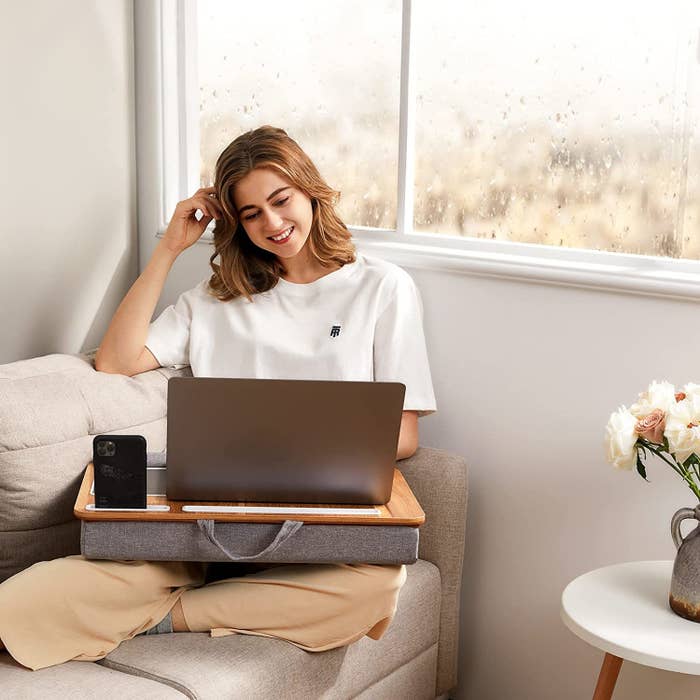 model sitting on couch using laptop with lap desk