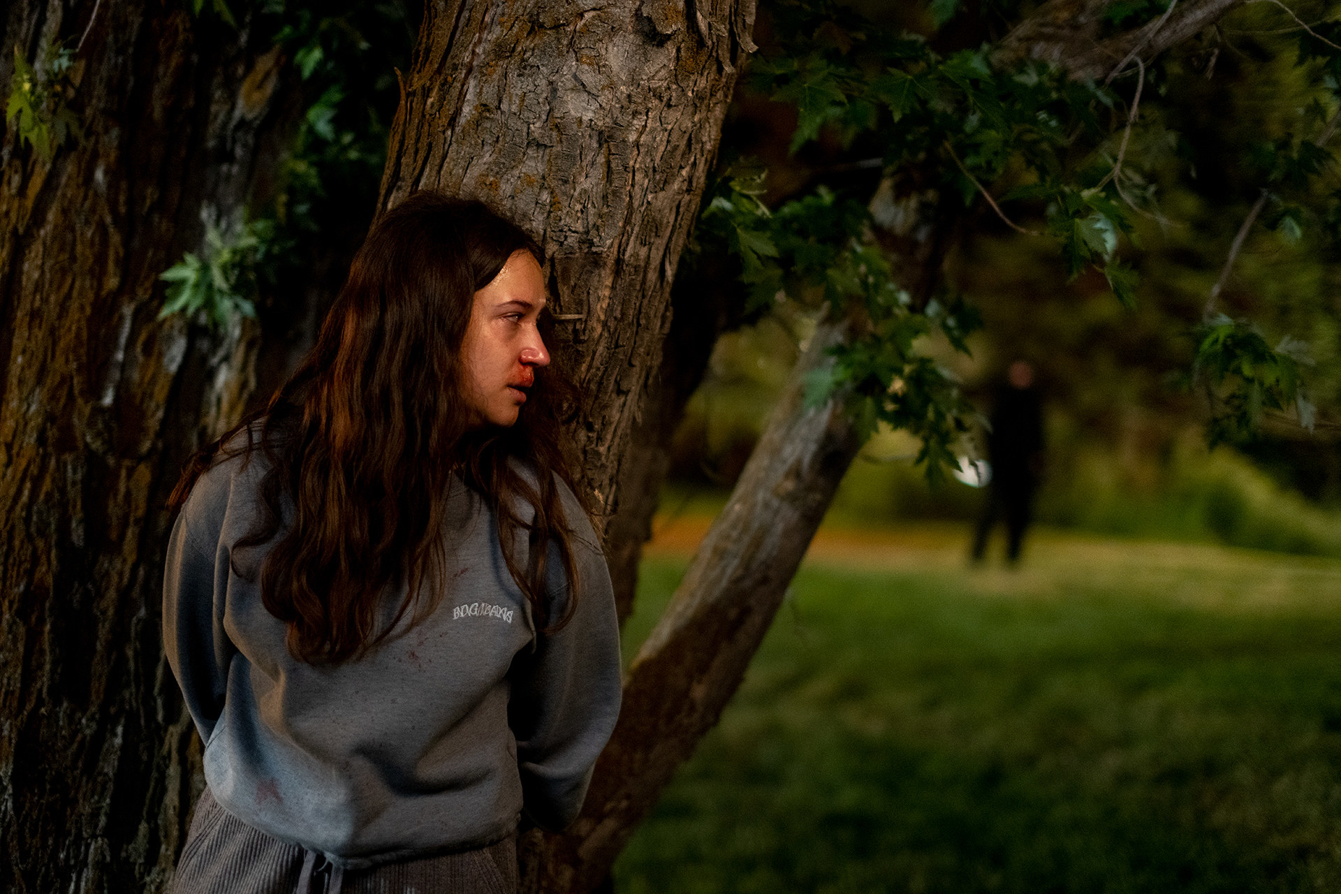 A young girl hides behind a tree while a killer stalks her