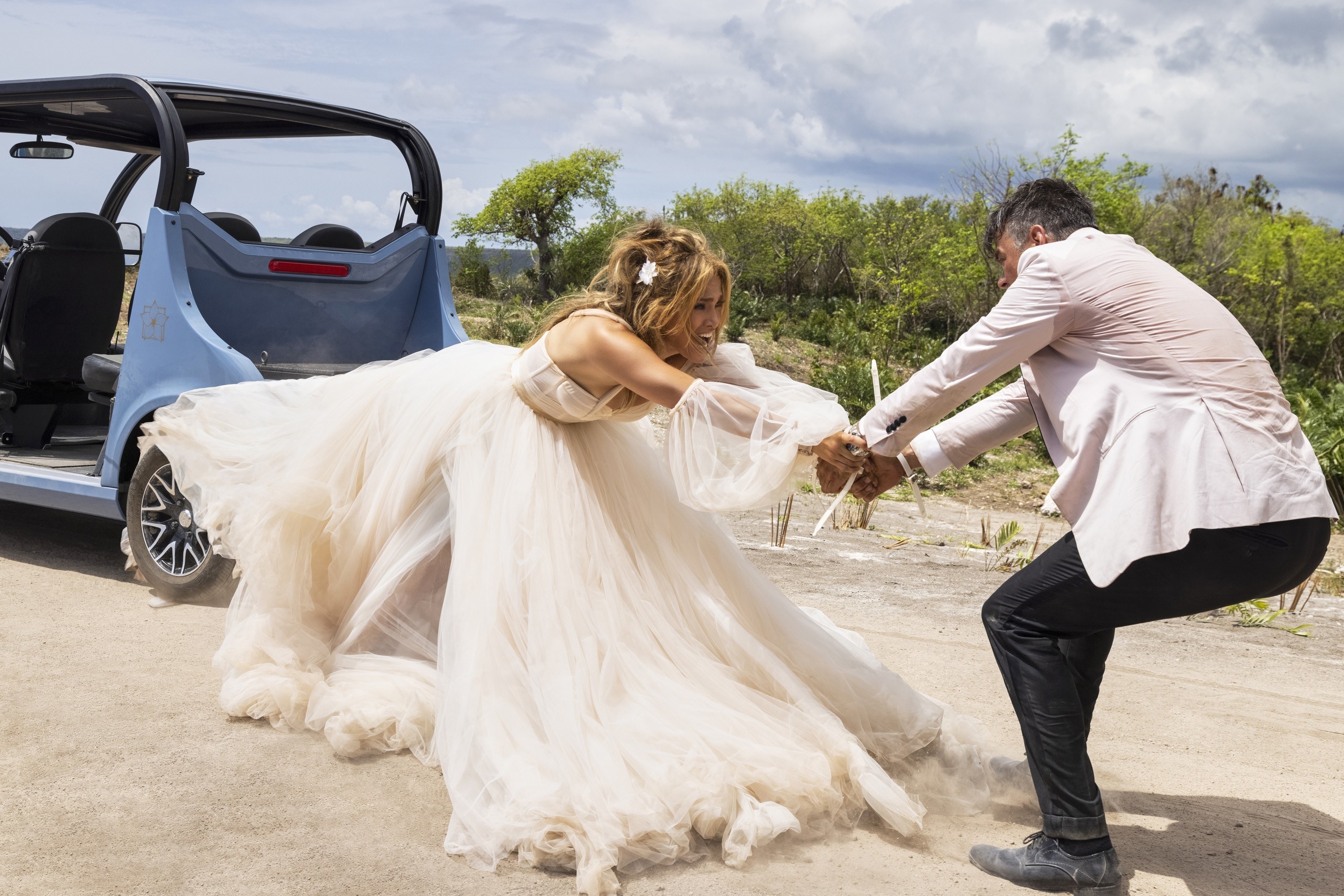 A man tries to pull a woman from a car, but her wedding gown is stuck