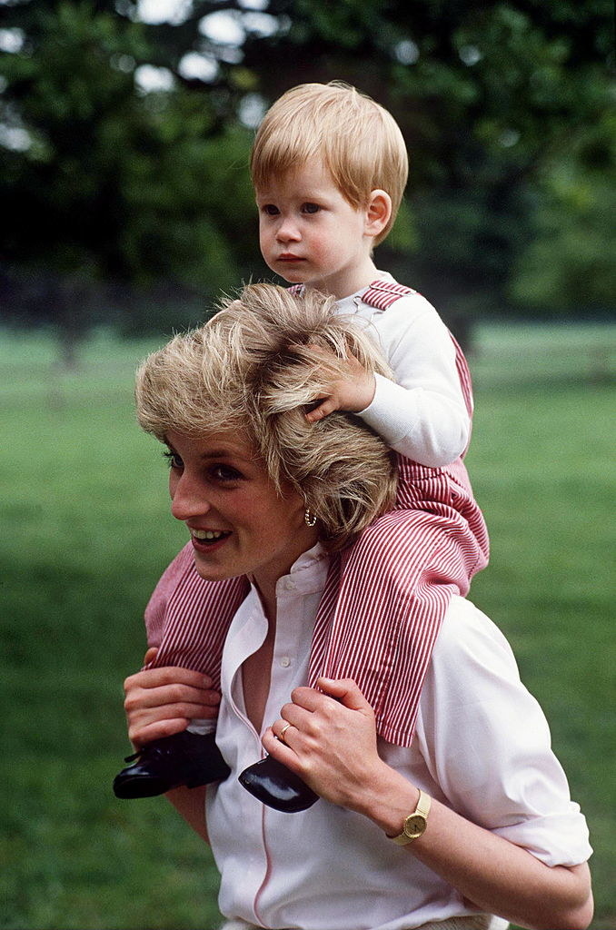 Princess Diana smiles as she carries a toddle Harry on her shoulders