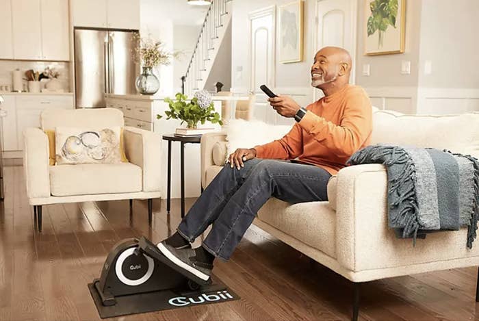 man watches TV while sitting on a couch and using the elliptical