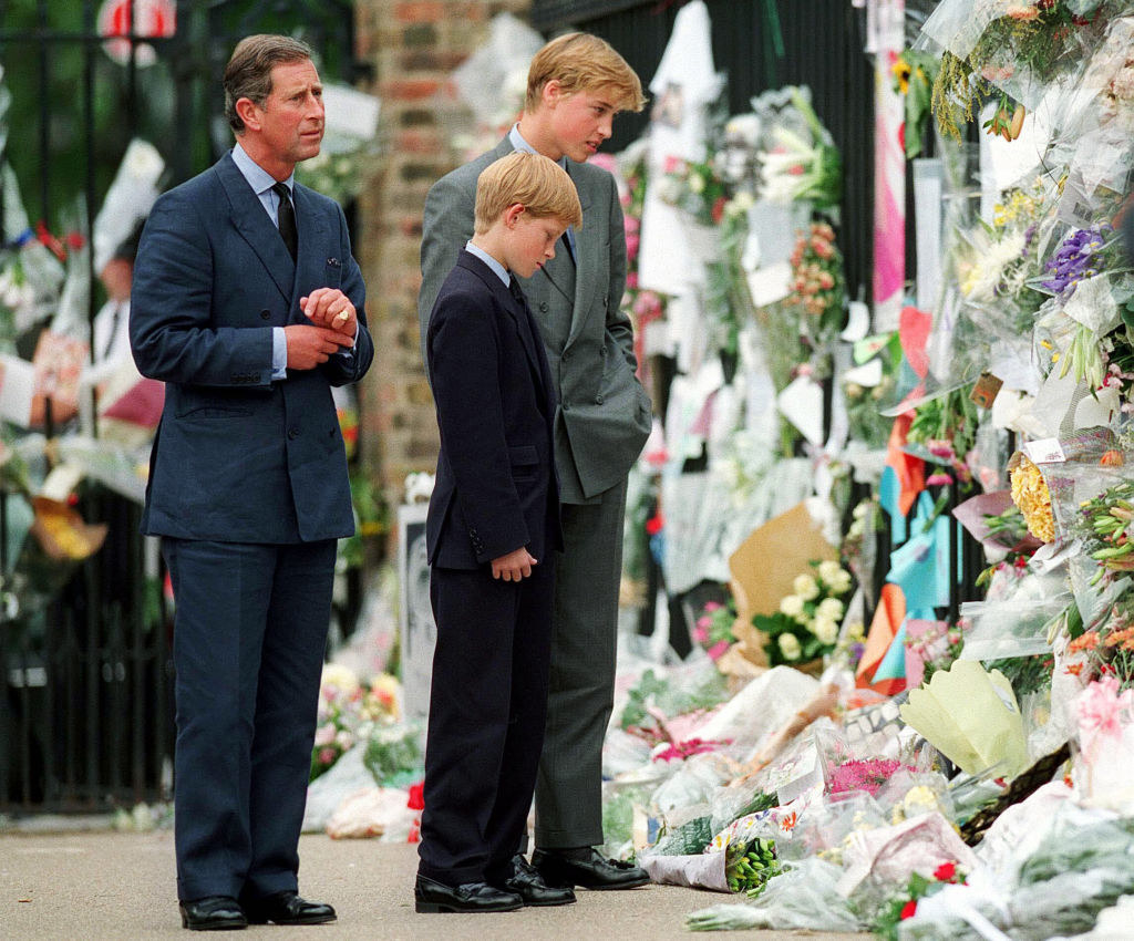 The two boys and their father looking at the flowers and cards left on a wrought-iron gate in tribute for their mother