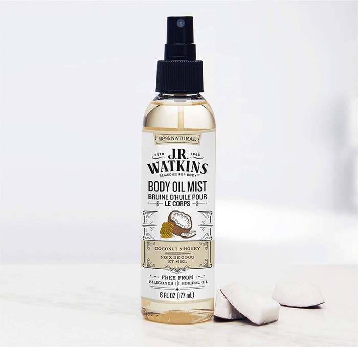 the body oil mist on a counter beside chunks of coconut