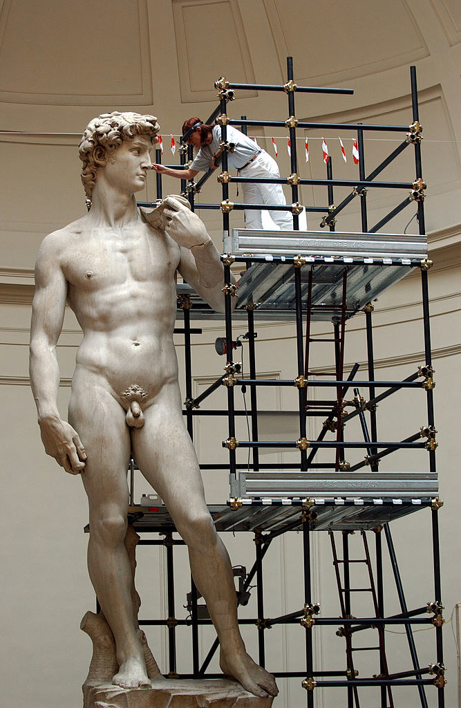 A person standing on tall scaffolding and working on David&#x27;s face