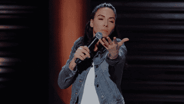 a gif of whitney cummings making a gimme gesture with her hands