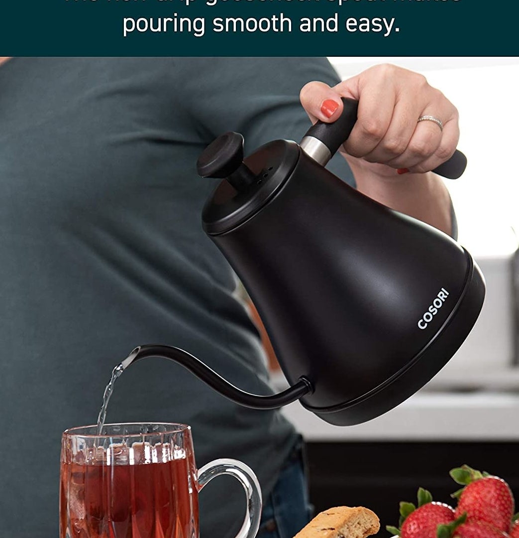 a person pouring water from the kettle into a glass mug