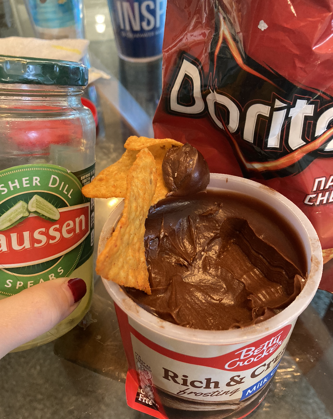 jar of pickles next to a tub of chocolate frosting with doritos being dipped in
