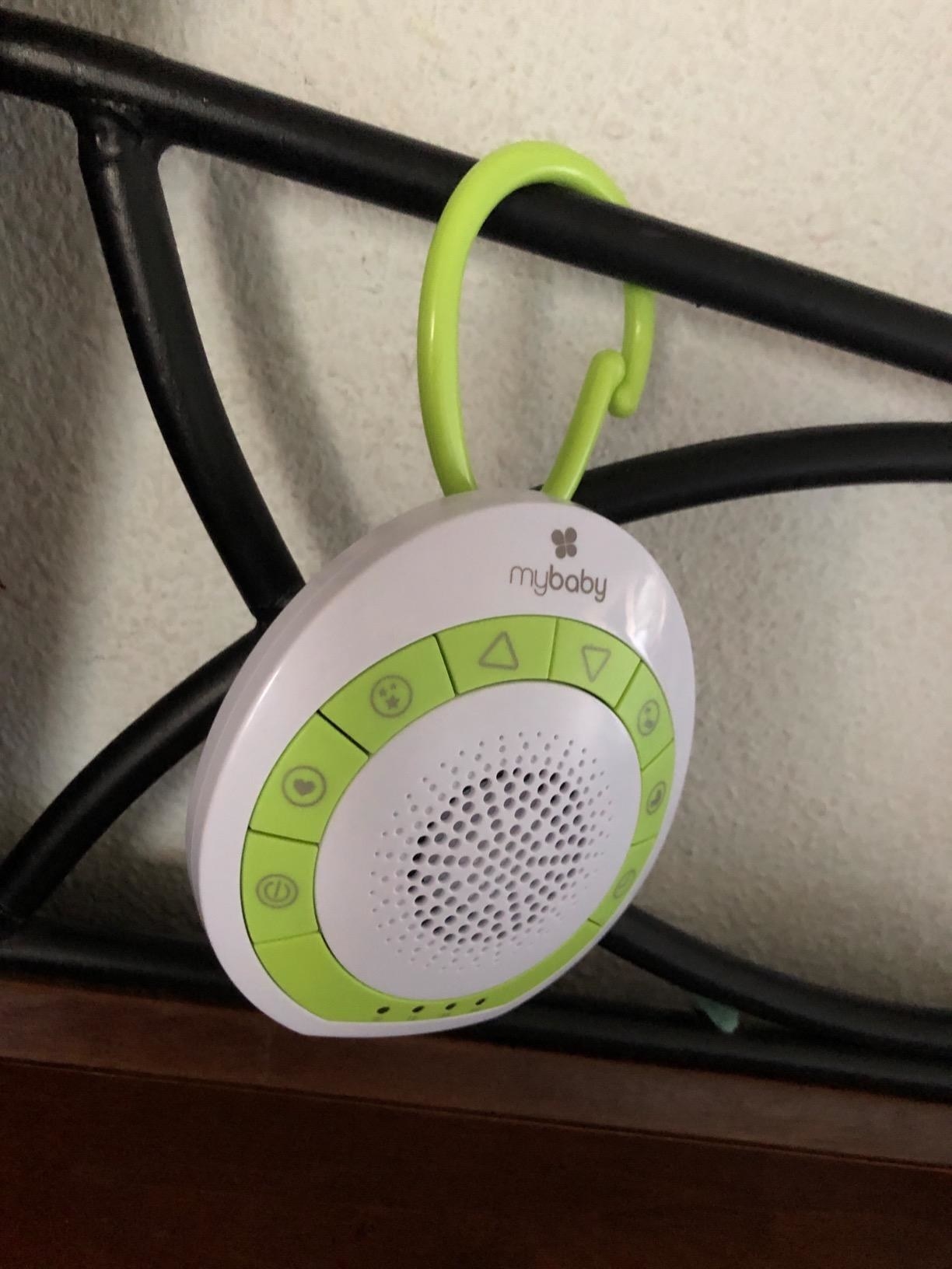 Reviewer&#x27;s small white and green noise machine clipped to their baby&#x27;s crib