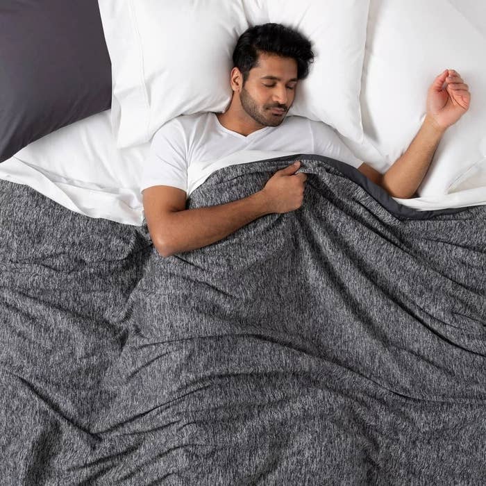 A model in a bed sleeping underneath a gray weighted blanket