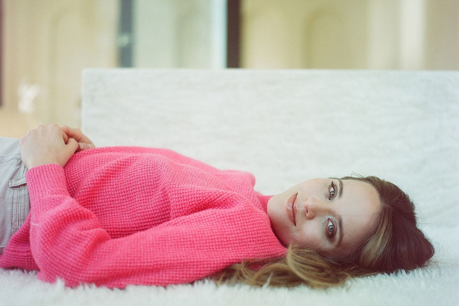 Vuolo lying down on white carpet in a bright pink sweater