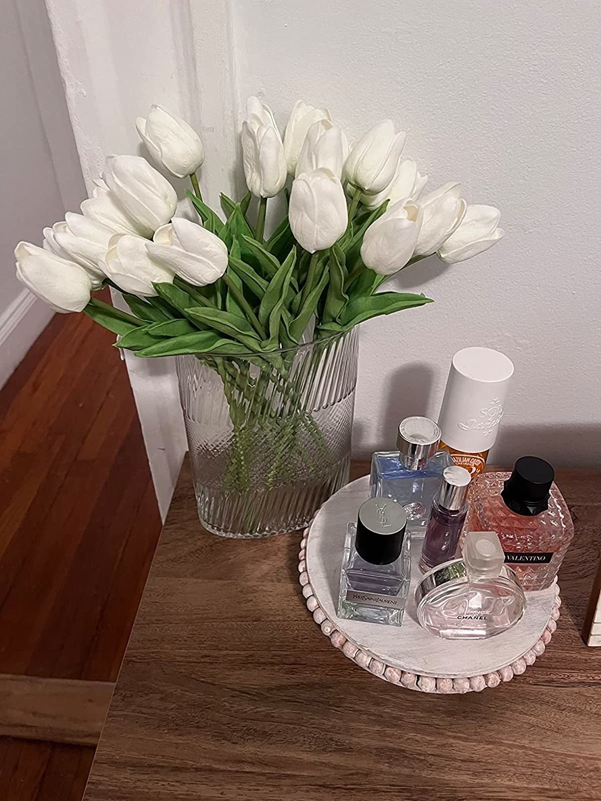 Reviewer image of white tulips in a vase next to a tray holding perfumes
