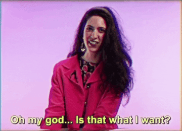 a woman with long hair in an 80s shoulder padded jacket laughing while saying oh my god is that what i want