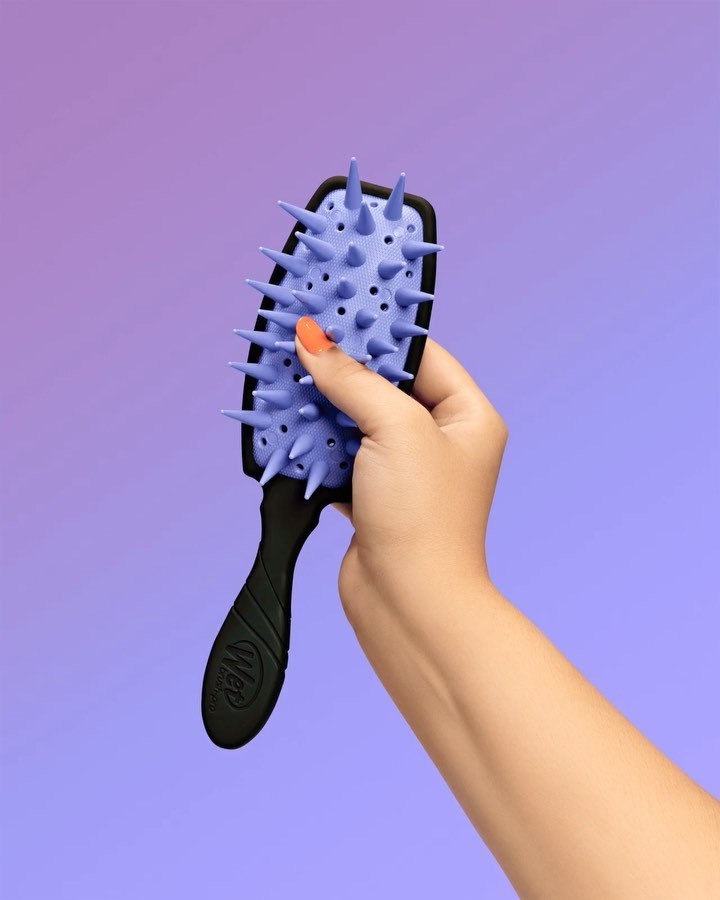 a person holding up the detangling brush and squishing it&#x27;s silicone bristles
