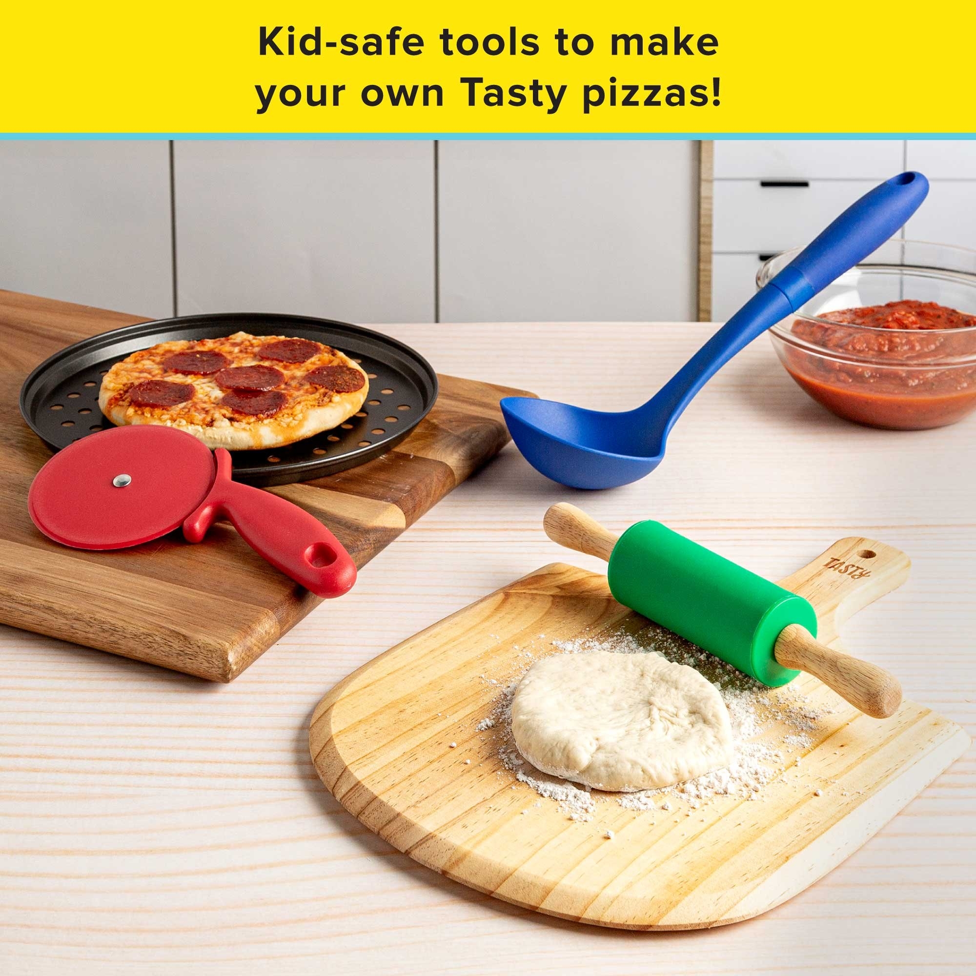 pizza pan next to red pizza cutter, green roller on serving board with dough, blue ladle next to bowl of sauce