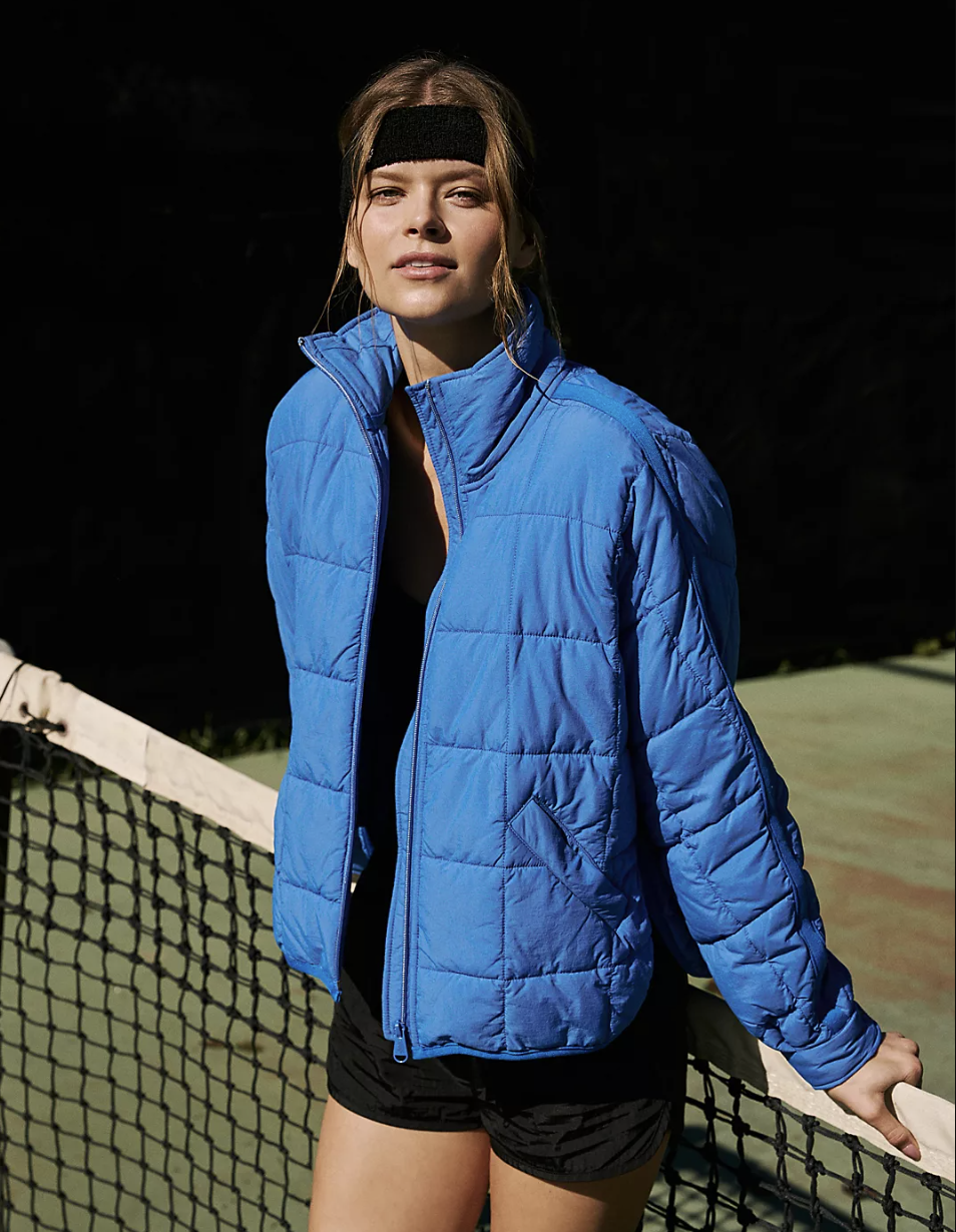 a smiling person on a tennis court while wearing the pullover puffer coat