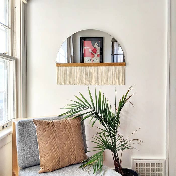 the fringe mirror hanging on a wall above a plant and accent chair