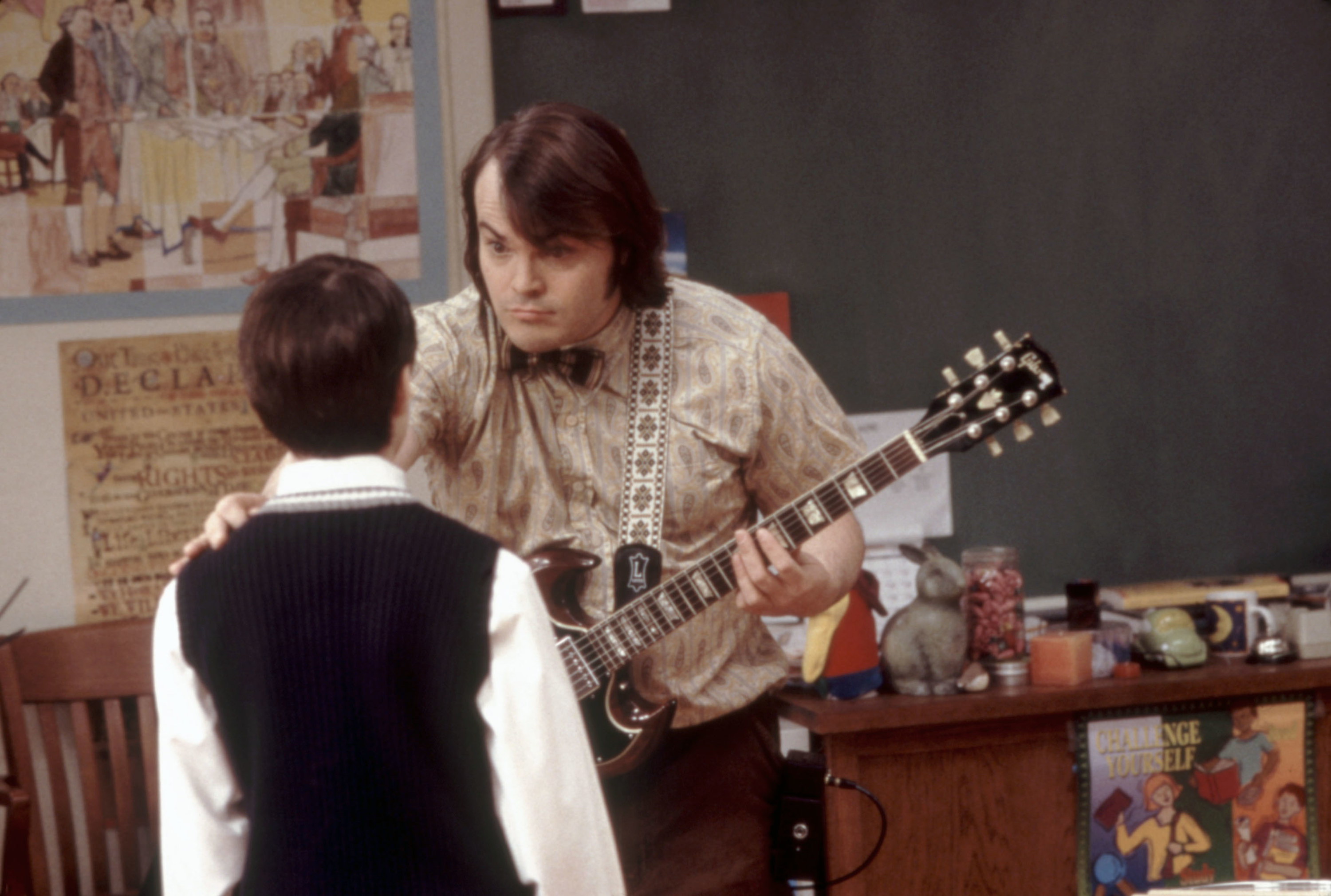 Jack in a classroom holding a guitar and looking at a student