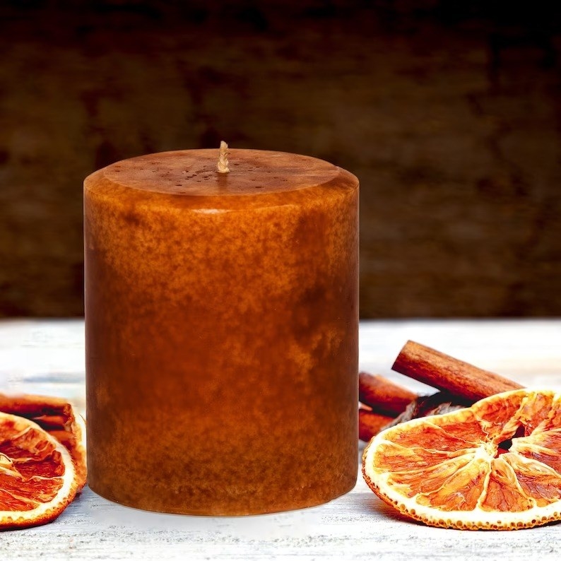 the small candle sitting beside cinnamon sticks and dried orange