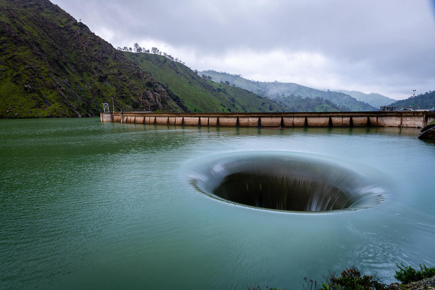 A whirlpool-type hole in the middle of a body of water surrounded by mountains