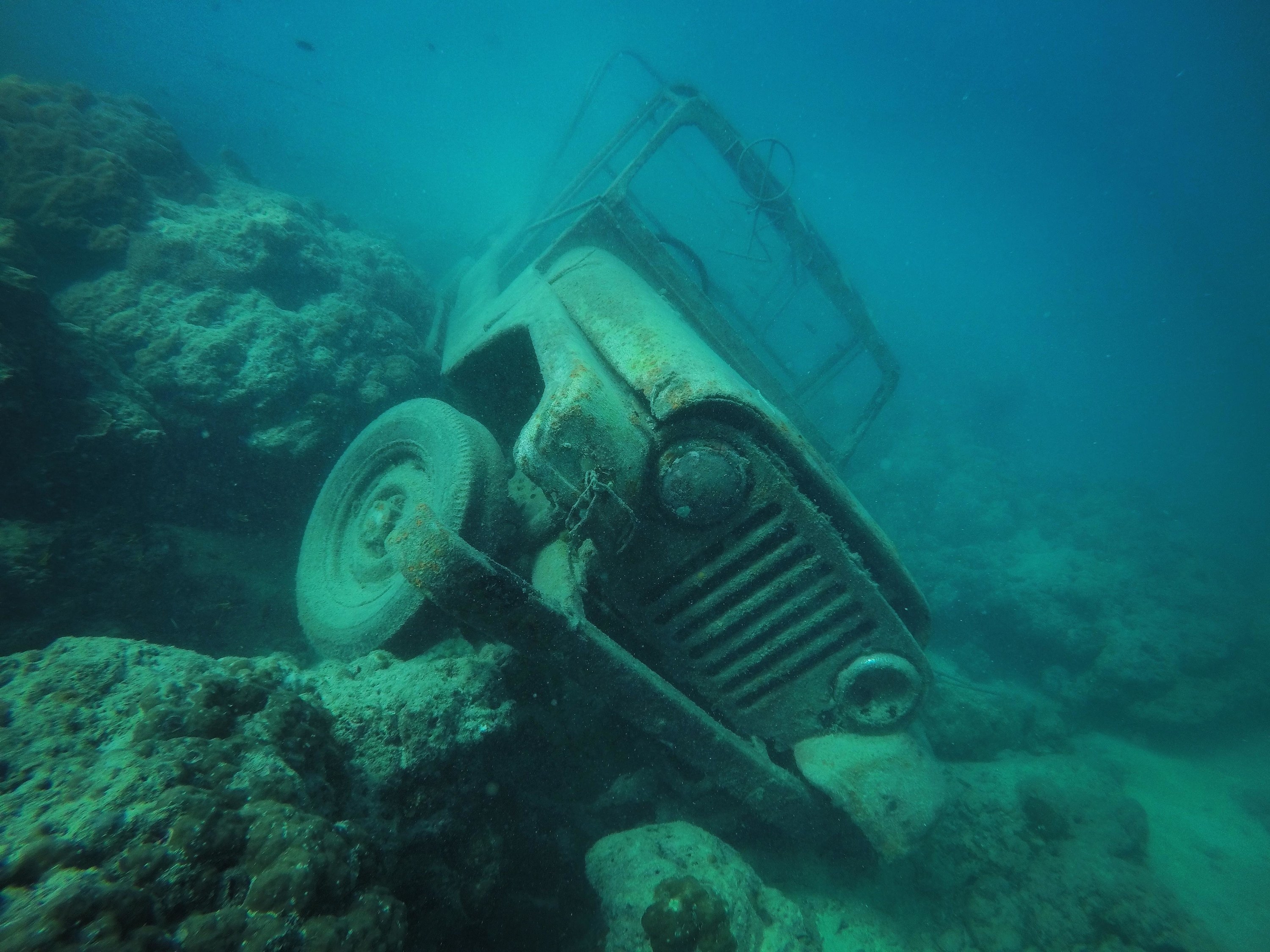 A rusted jeep resting on rocks at the bottom of the water