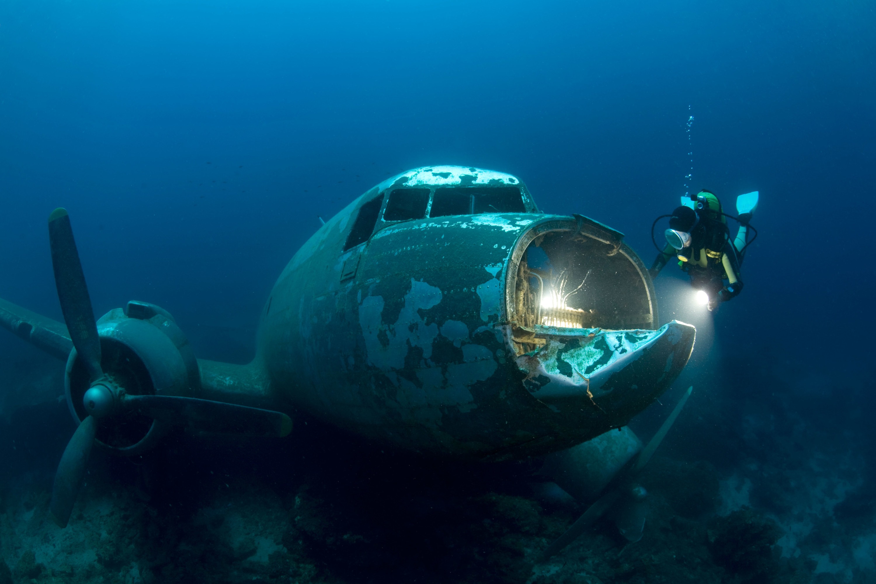 A propeller plane underwater, with a diver looking at it with a flashlight