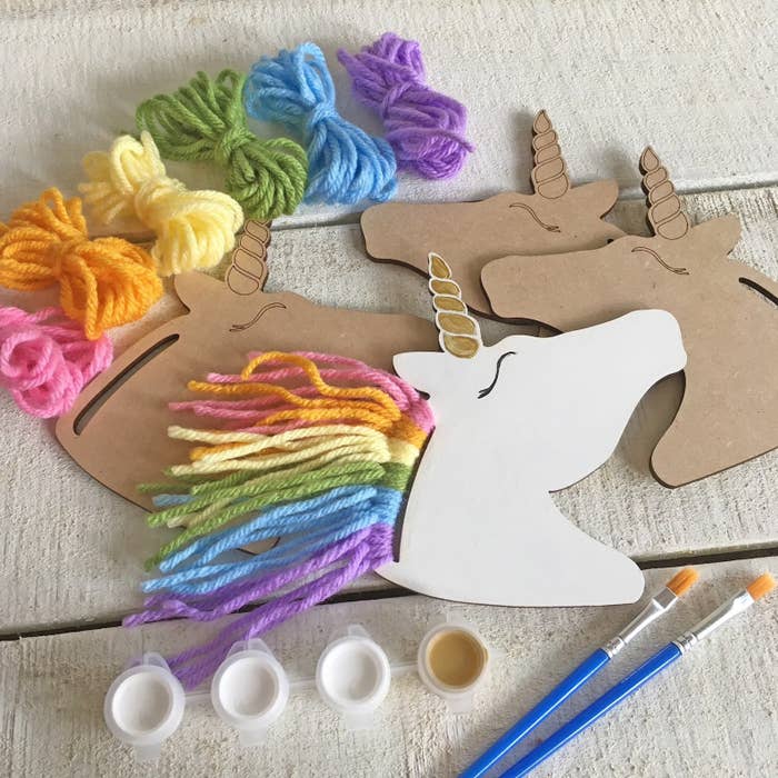 White and cardboard unicorn crafts with colorful yarn, paint, and brushes