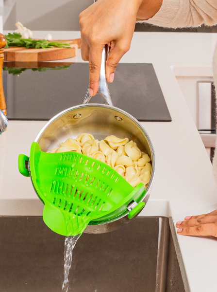 A model straining pasta from a green strainer clipped to the sides of the pot
