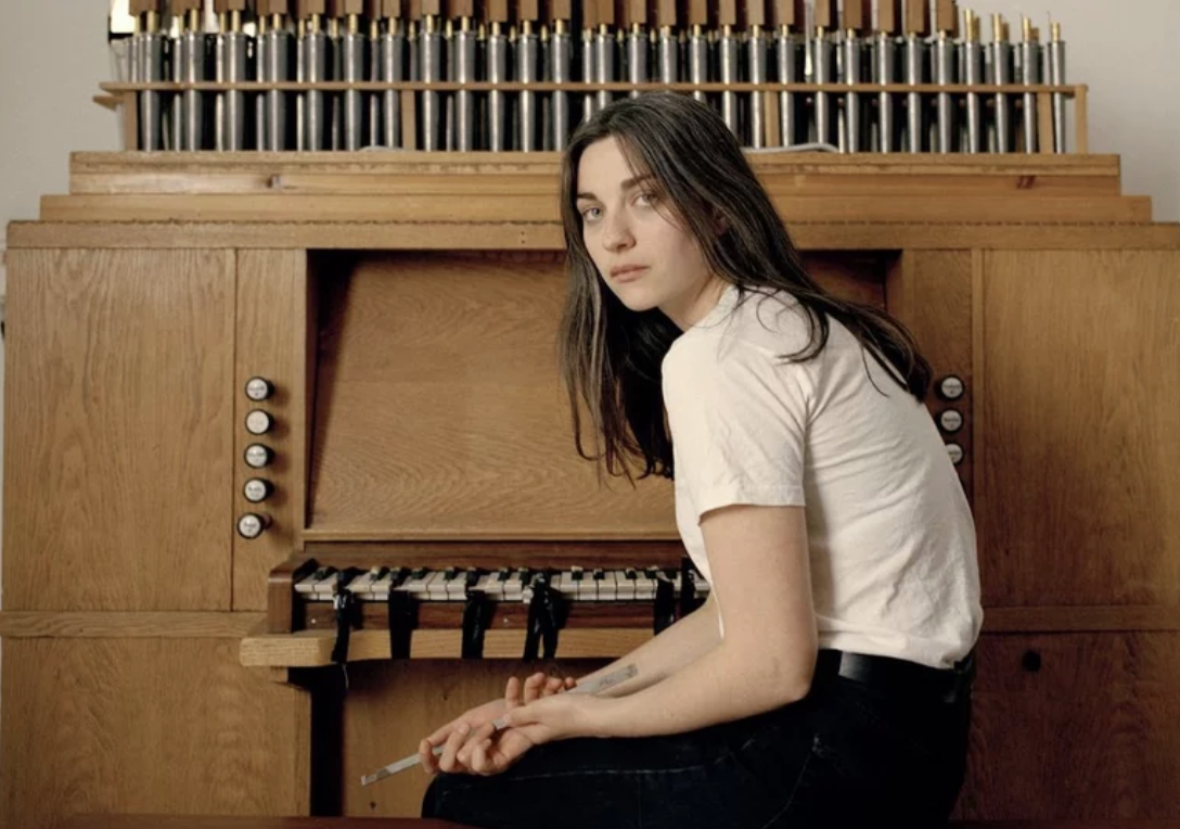 Kari Malone leans over sitting in front of a tan brown piano