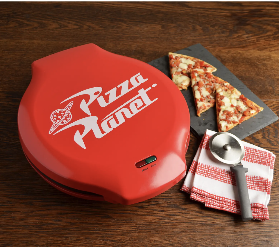 pizza maker with pizza planet logo printed on it, next to three slices of pizza on a plate and a pizza cutter