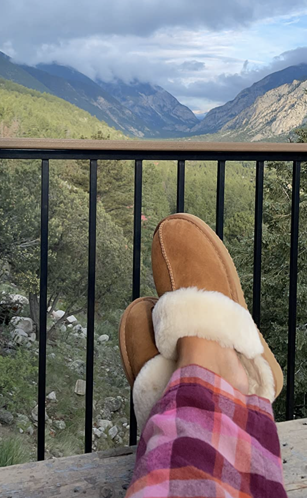 A reviewer wearing the chestnut slippers with a mountain view behind
