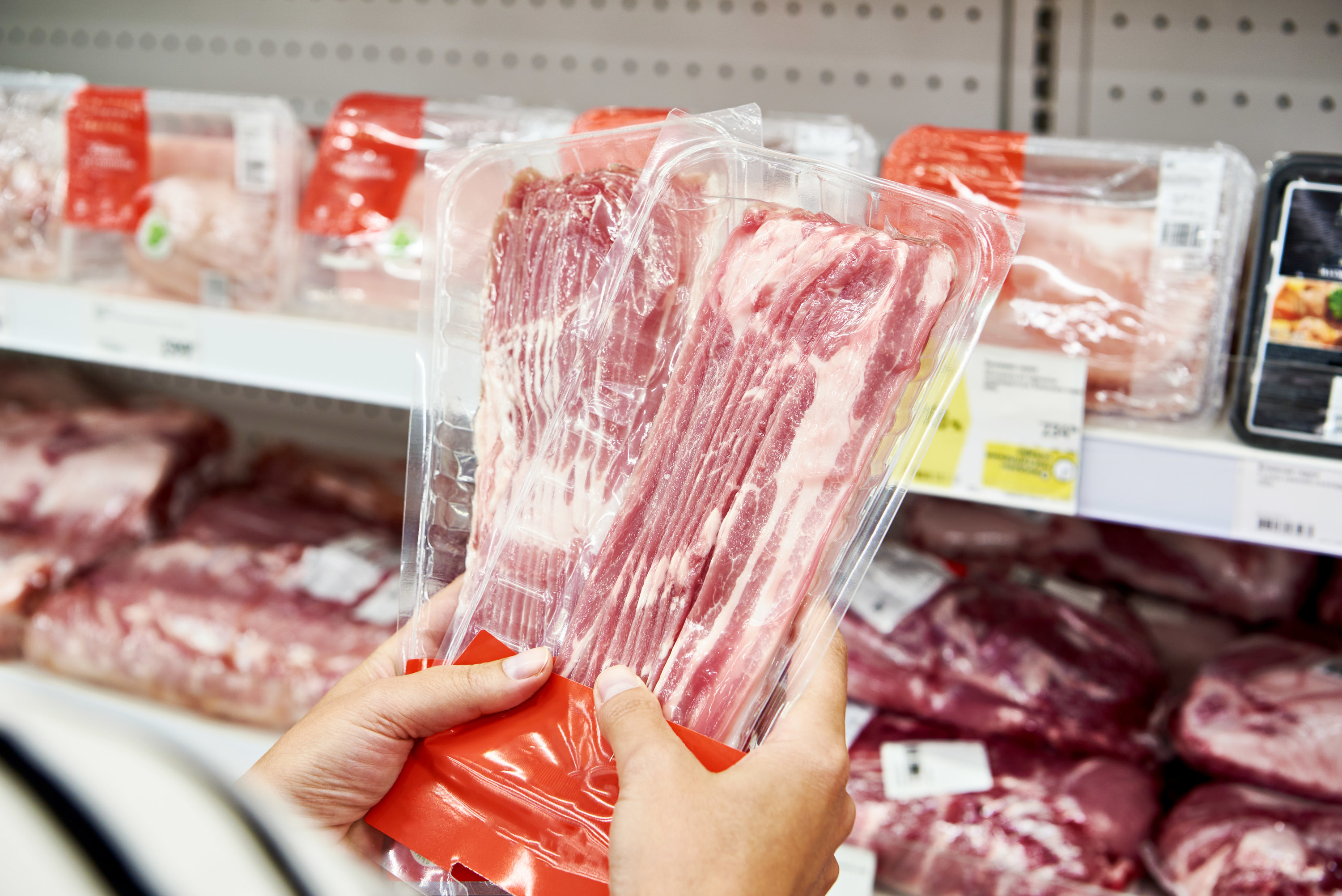 Woman chooses a slice of pork meat in vacuum package at the grocery store