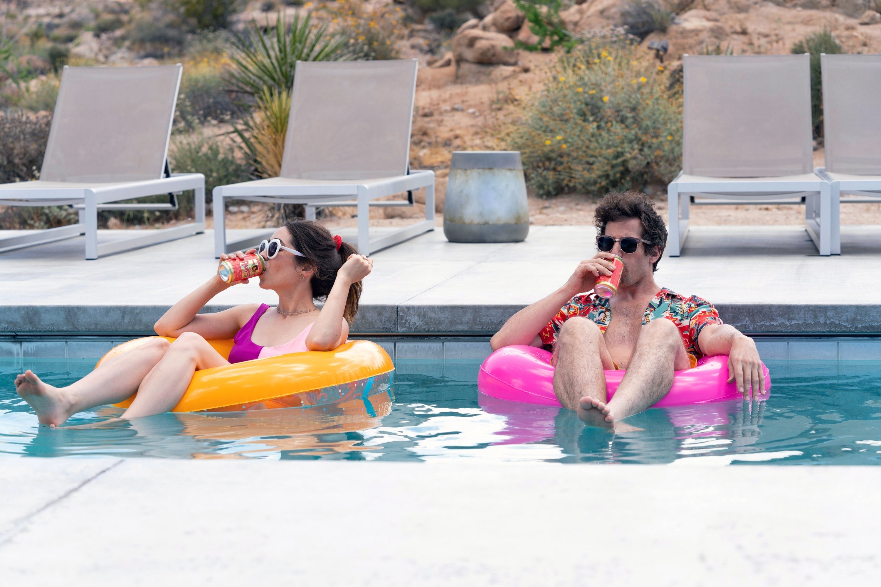 Sarah and Niles drink beverages while sitting in floaties in a pool