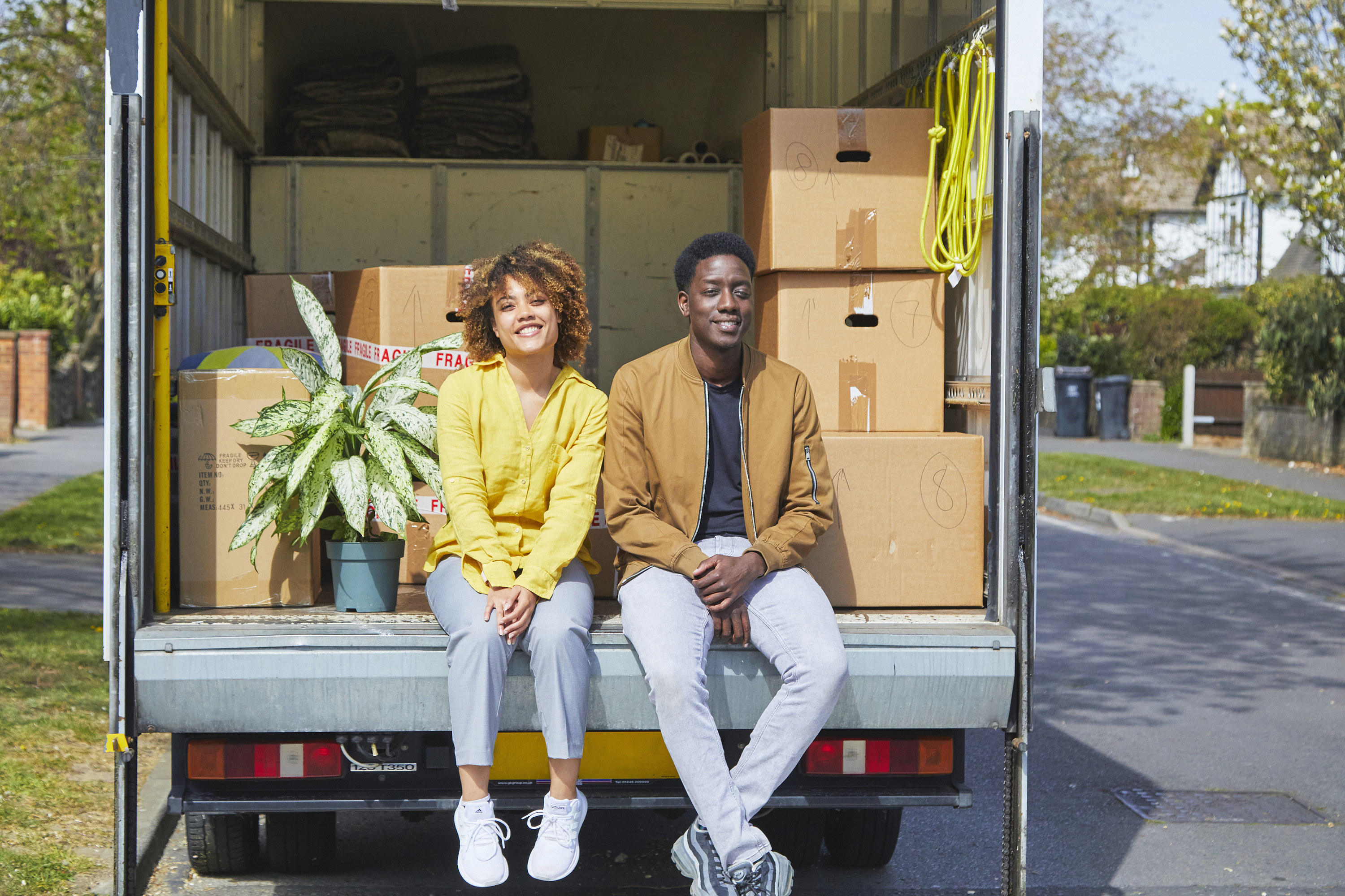 couple sitting in their moving truck with boxes behind them in front of their new house