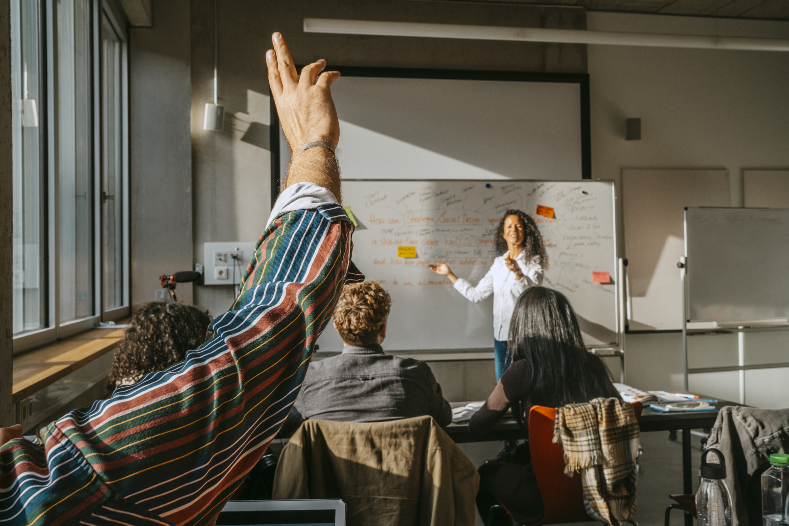 student raising their hand in a college classroom