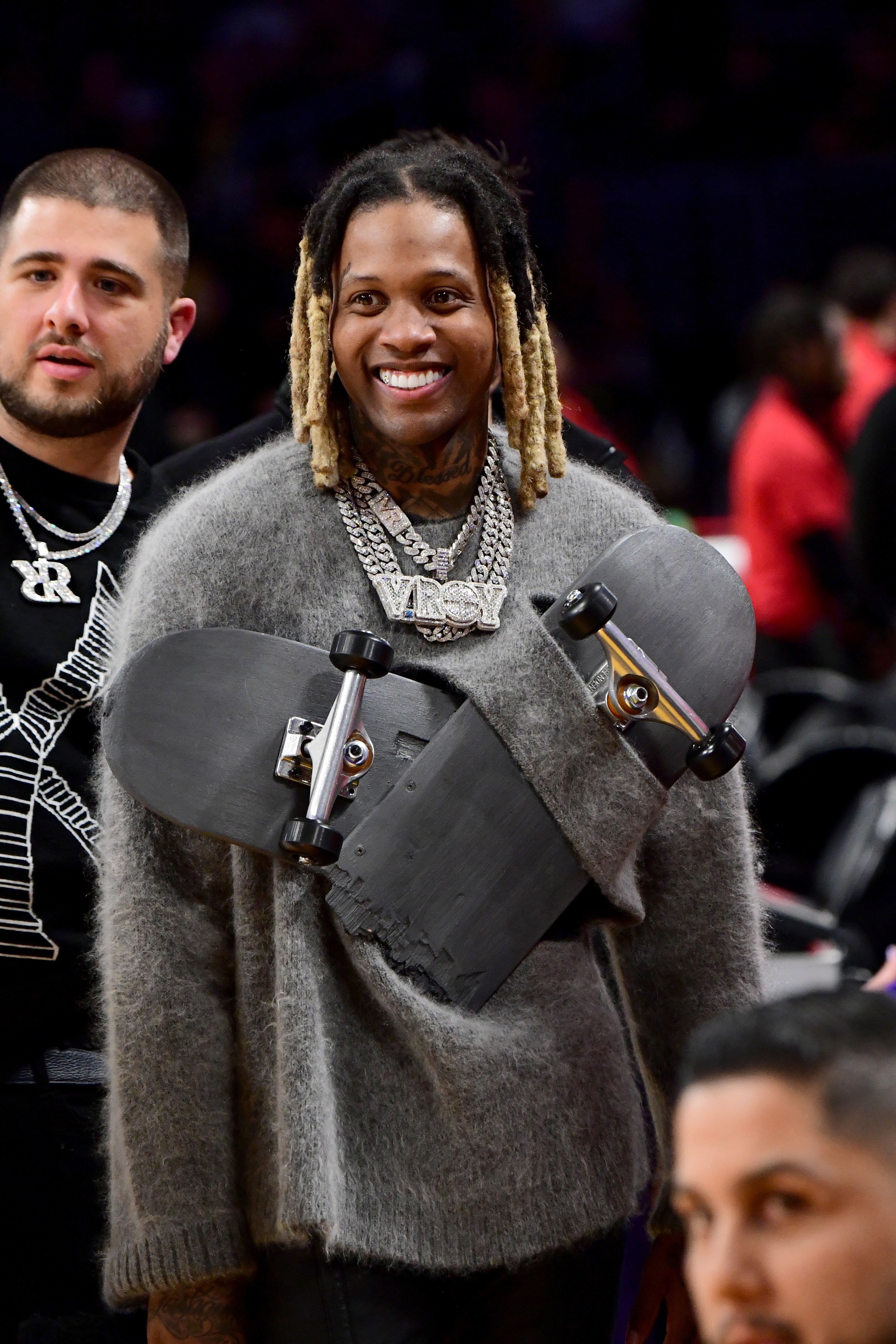 lil durk smiling in the sweater with the broken skateboard attached