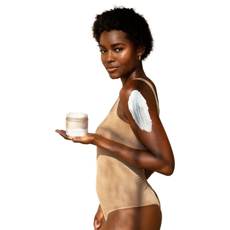 A person with a short afro holding a jar of body butter with a swatch on their arm