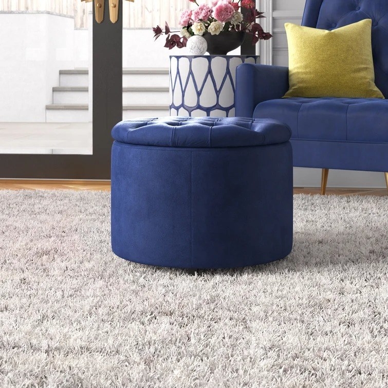 The blue ottoman sitting atop a light-colored tufted rug with a blue couch behind
