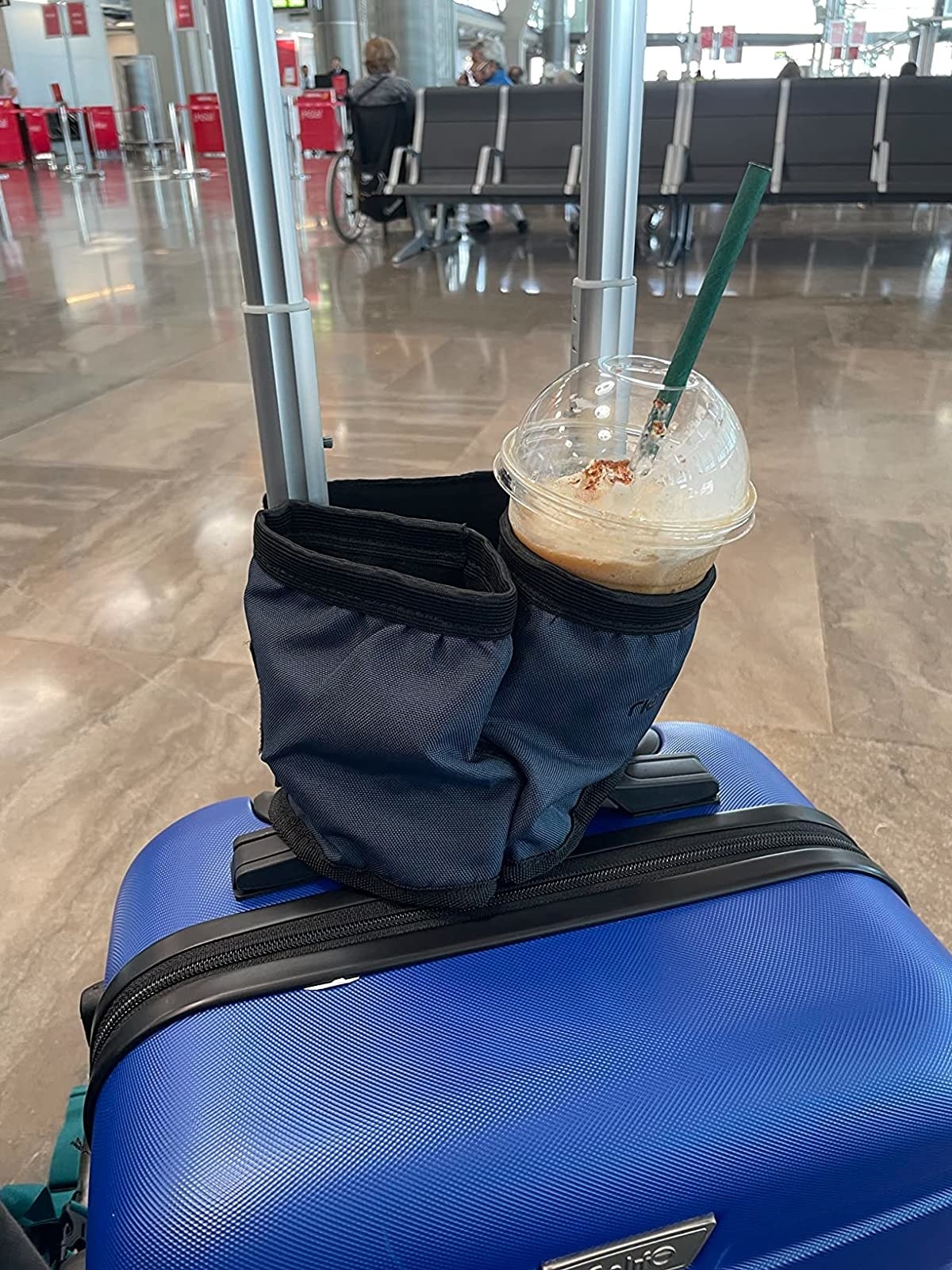 Reviewer&#x27;s blue suitcase with iced coffee in one pocket of the two-pocket cup holder attached to luggage handle