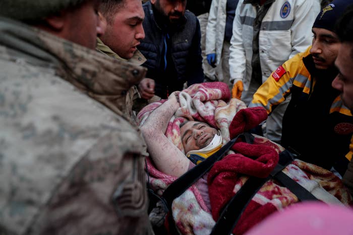 A person with their eyes closed is covered in blankets and surrounded by rescuers