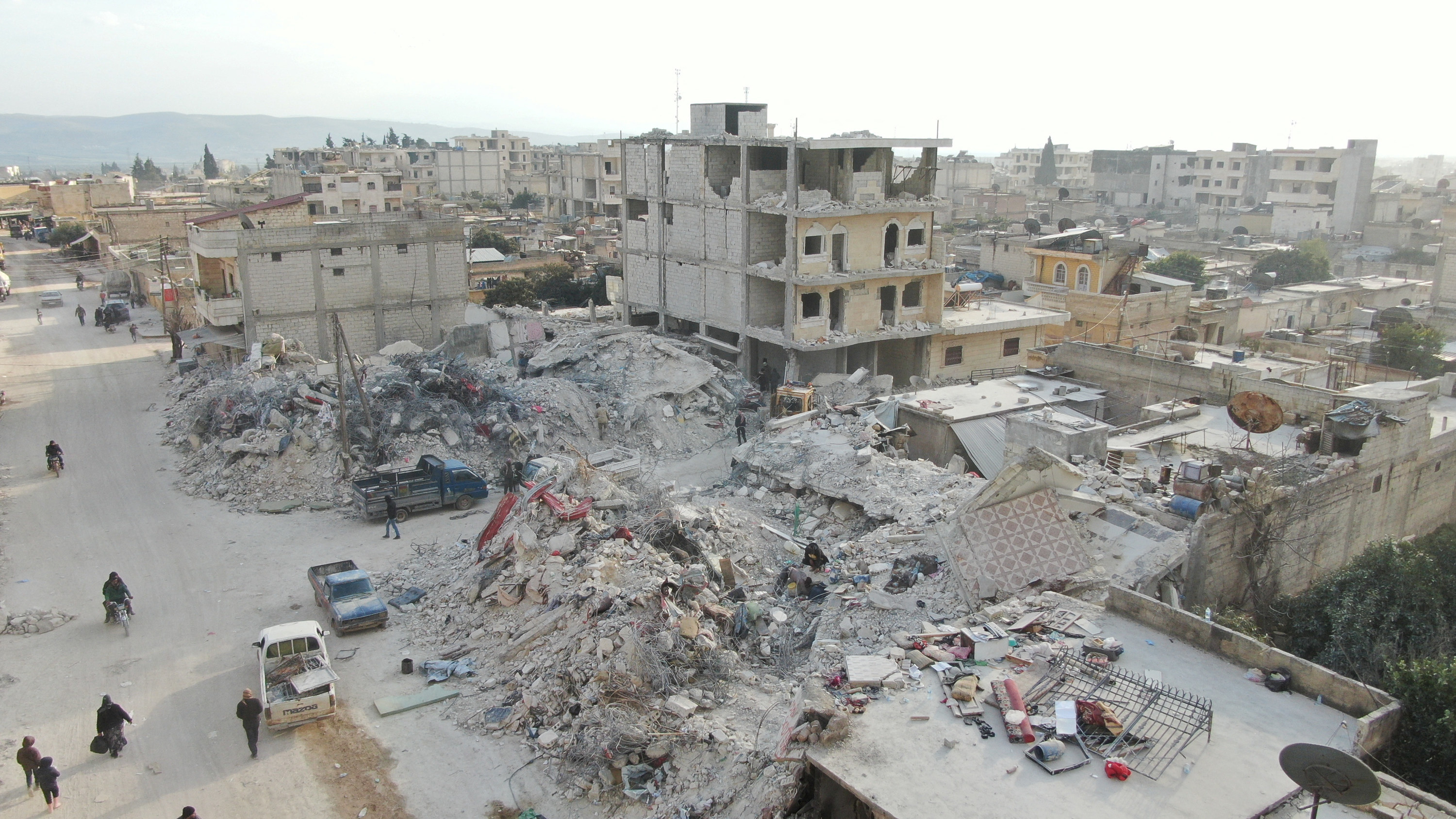 A view of collapsed buildings and a few people walking amid the rubble