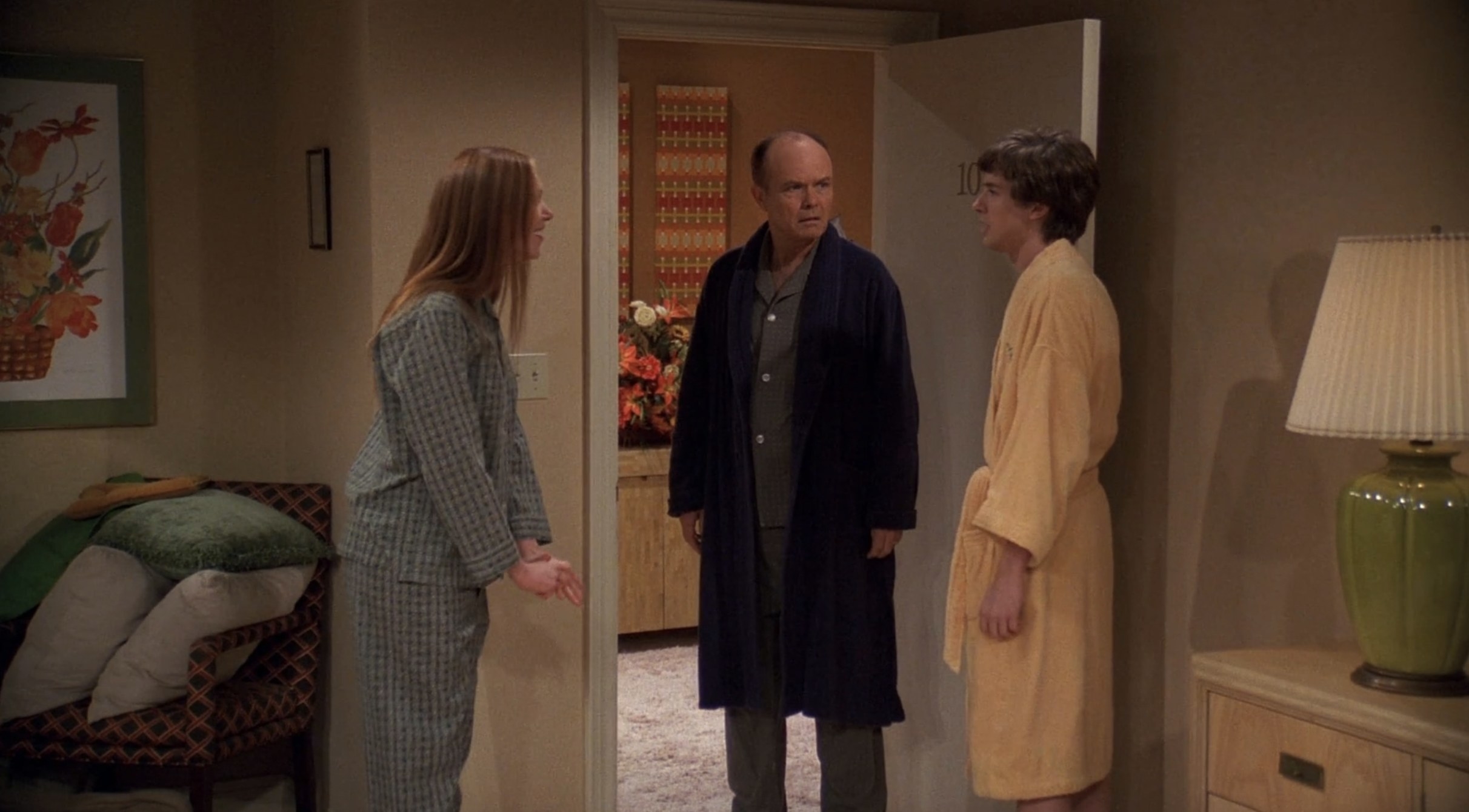 Eric and Donna stand in a robe and pajamas, while Red looks at them disapprovingly