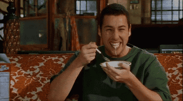 Adam Sandler eating cereal on a couch.