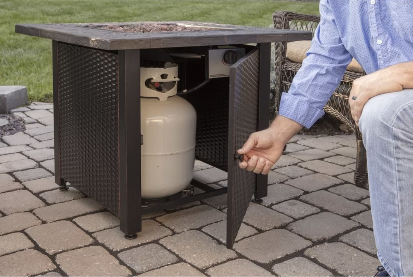 A black fire pit table with someone opening the bottom to show a propane tank