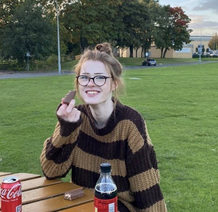 Brianna Ghey, a smiling red headed girl, holds a candy bar in the park.